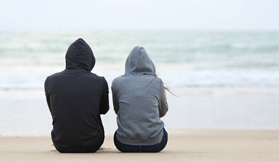 Two people sat on the floor with hoods up