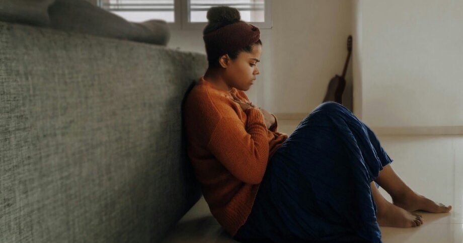 Woman clutching her chest, sat on the floor.