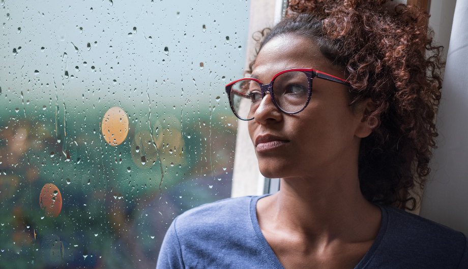 A woman wearing glasses looking out a window.