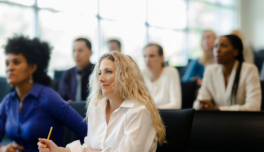 A woman and fellow learners listening to and watching a trainer teaching a course.